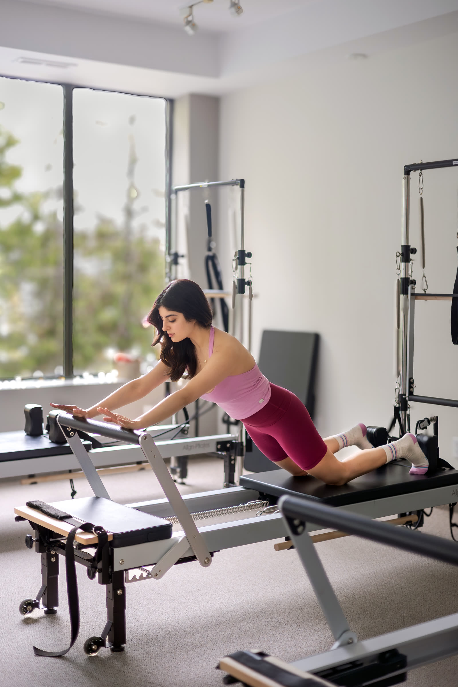 Juhi on a Reformer by a window, arms extended to the footbar